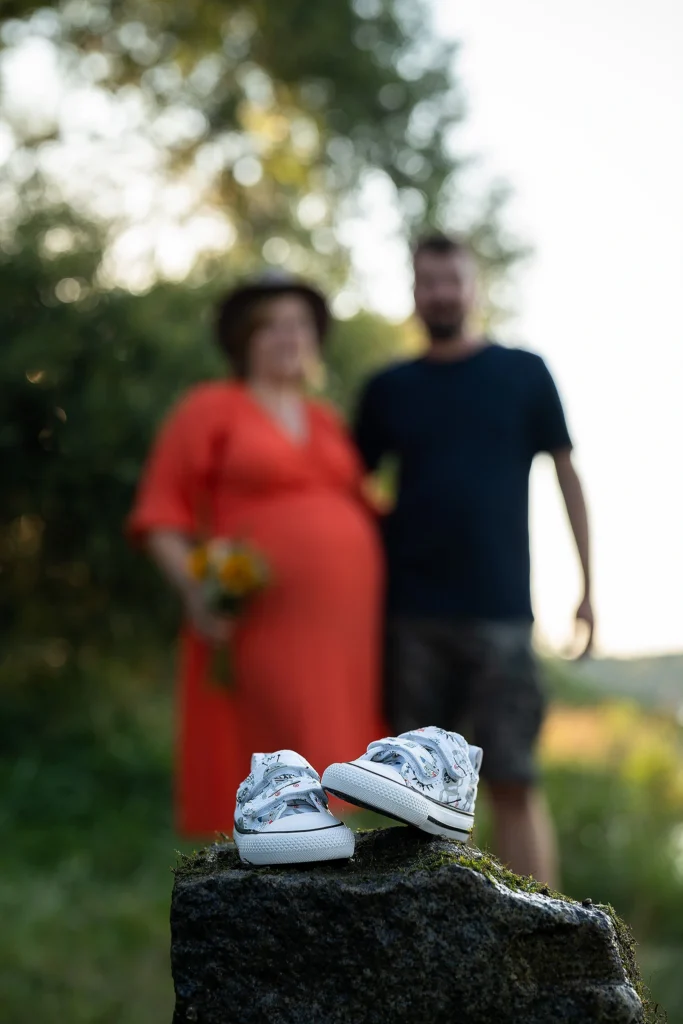 kleine Schuhe für ein zukünftiges Baby im Vordergrund, im Hintergrund erahnt man die angehenden Eltern