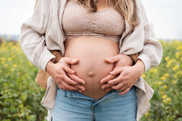 Nahaufnahme vom Babybauch. Mann umarmt Frau von hinten und beide haben ihre Hände am Bauch.