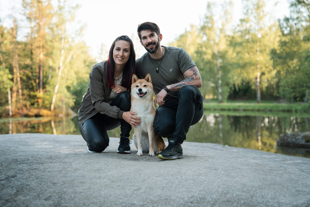 Pärchen kniet am Boden mit Hund beim Sonnenuntergang